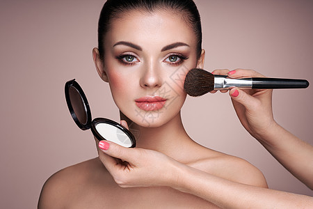 美丽的女人用刷子涂肤色漂亮的女人脸完美的妆容护肤基金会刷化妆师背景图片