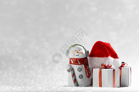 带圣诞帽的雪人圣诞快乐新年贺卡快乐的雪人站圣诞礼物圣诞老人的帽子上银色的闪光背景带圣诞礼物圣诞帽的雪人背景
