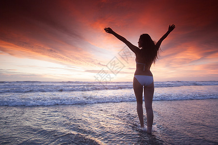 穿着比基尼的女人举起手臂,走向美丽的夕阳海上海上日落的女人图片