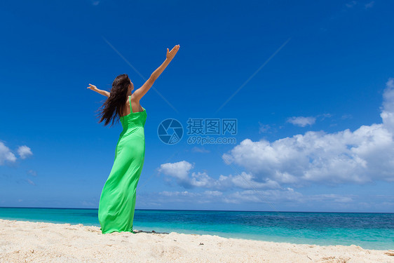 穿着绿色连衣裙的女人热带海滩上摆姿势,举起手臂海滩上穿裙子的女人图片