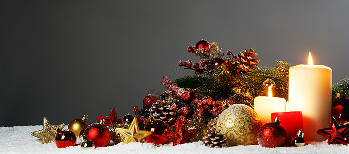 雪地上点燃圣诞蜡烛,上面有红色金色的装饰星装饰品松果绿色的树枝装饰圣诞蜡烛图片
