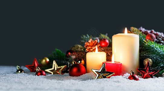雪地上点燃圣诞蜡烛,上面有红色金色的装饰星装饰品松果绿色的树枝装饰圣诞蜡烛图片