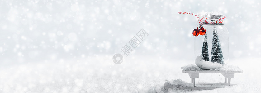 圣诞装饰玻璃罐与条纹丝带,铃铛杉树玩具雪橇雪背景雪上的圣诞装饰品图片
