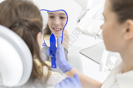 牙医牙科诊所向微笑的女孩病人展示镜子图片