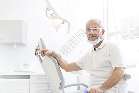 自信的资深牙医坐牙科诊所的椅子上的肖像图片
