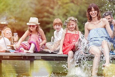 微笑的女人女儿湖边泼水,而坐码头上与家人夏季野餐图片