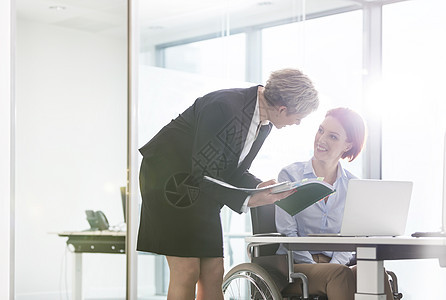 成熟的女商人与办公室办公桌上的残疾同事讨论文件图片