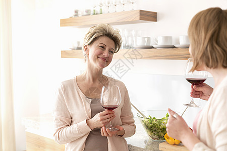 微笑的成熟女人站厨房里着酒杯图片