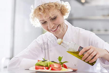 微笑成熟的厨师餐厅的盘子里浇油沙拉图片