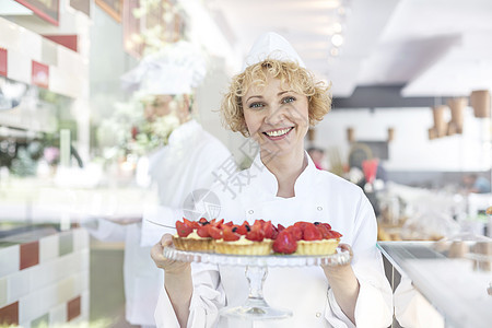 微笑的成熟厨师餐厅的托盘里着新鲜的草莓馅饼的肖像图片