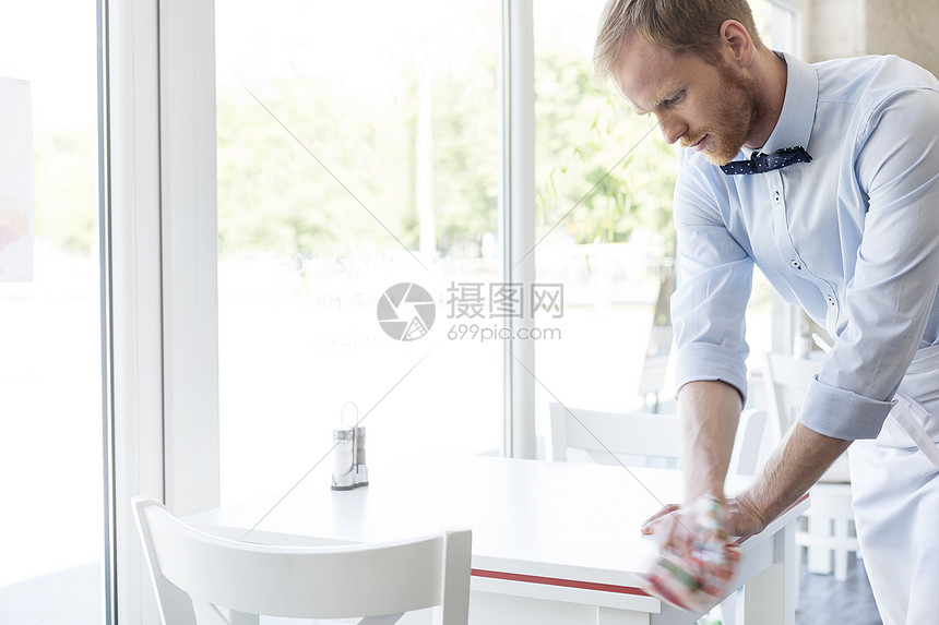 自信的年轻服务员餐厅擦桌子图片