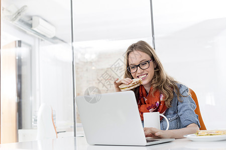 创造的女商人办公室用笔记本电脑吃早餐图片