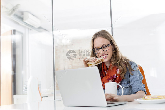 创造的女商人办公室用笔记本电脑吃早餐图片
