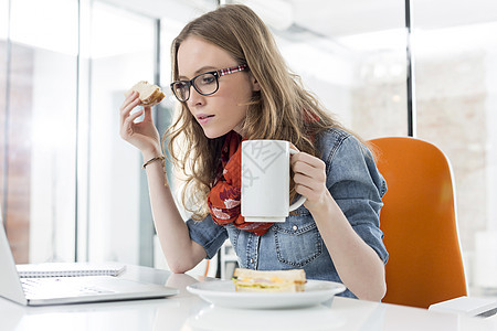 女商人办公室吃早餐时用笔记本电脑图片