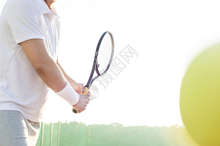 成年男子蓝天上打网球的中段图片