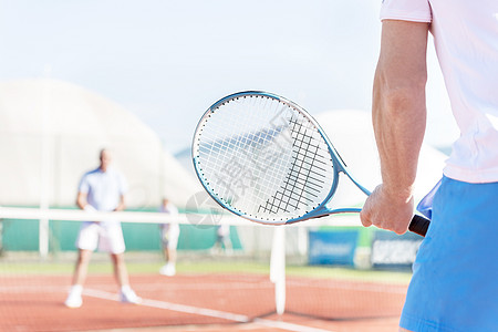 成年男子网球场上与朋友起玩球拍的中段图片