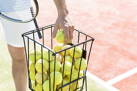 阳光明媚的日子里,男人金属篮子里捡网球的中段图片
