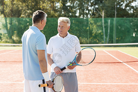 成熟的男人着球拍,夏天的周末网球场上聊天图片