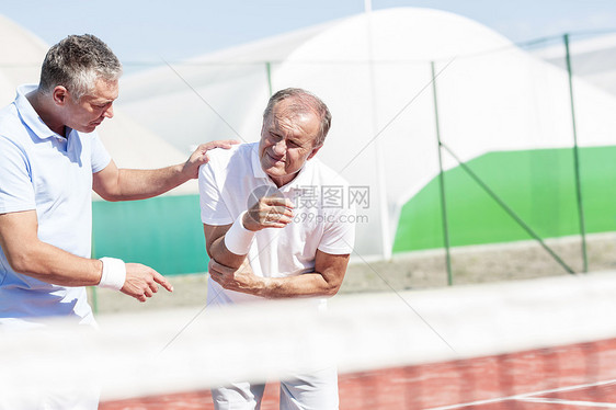 成熟的男人阳光明媚的日子里打网球,帮助资深朋友肘部受伤图片