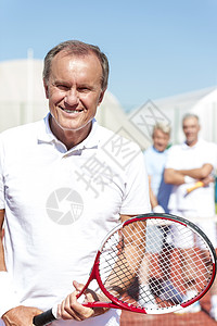 阳光明媚的天,微笑的老人手持网球拍,球场上与成熟的朋友站起图片