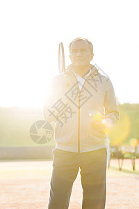 阳光明媚的日子里,年长的男人着网球拍球站晴朗的天空上图片