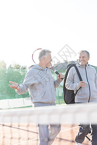 穿着运动服的微笑的男人网球场上着晴朗的天空说话图片