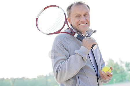 微笑的退休老人的肖像,站网球拍球着晴朗的天空阳光明媚的日子图片