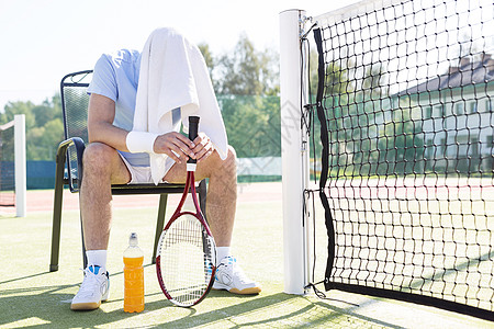阳光明媚的天,网球场上,全身疲惫的成熟男人戴着覆盖的头坐椅子上图片