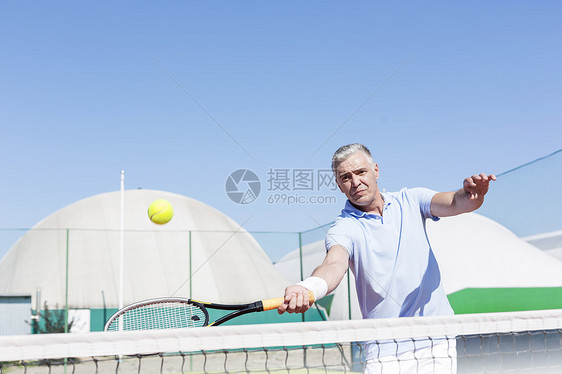 自信的成熟男人用球拍球场上着晴朗的蓝天打网球图片