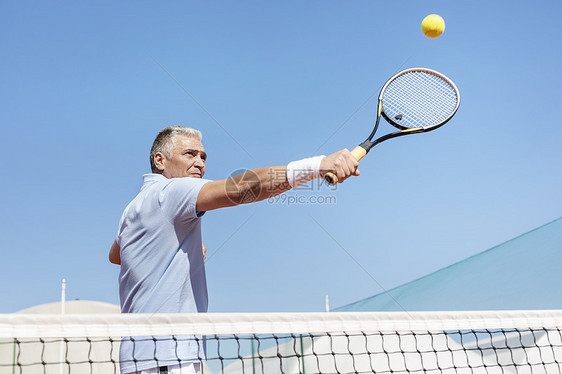 自信成熟的男人用球拍球场上着晴朗的蓝天打网球的低角度视角图片