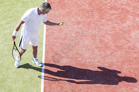 阳光明媚的天,自信成熟的男人网球场上发球的高角度观点图片