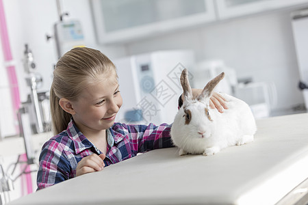 微笑可爱的女孩看着兽医诊所床上的兔子图片
