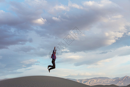 日落时沙丘上跳跃的人图片