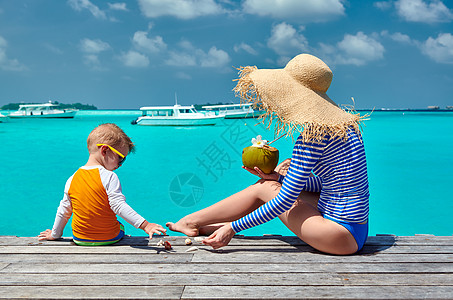 三岁的蹒跚学步的男孩,母亲坐木制码头上马尔代夫的暑假家庭假期图片