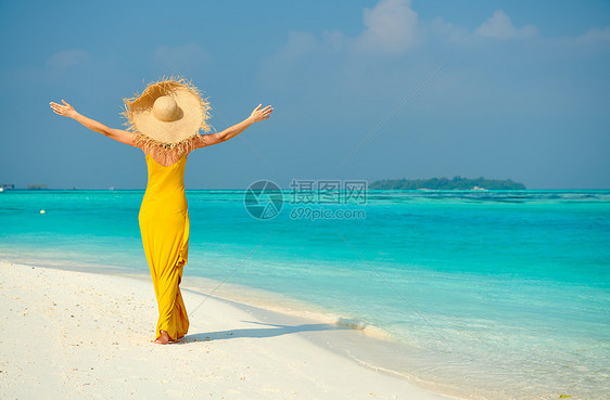 穿着连衣裙的女人热带海滩上散步,双臂伸出马尔代夫的暑假图片