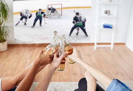 体育娱乐活动人们的快乐的朋友家里的投影仪屏幕上碰碰啤酒瓶看冰球比赛朋友们看冰球喝啤酒图片