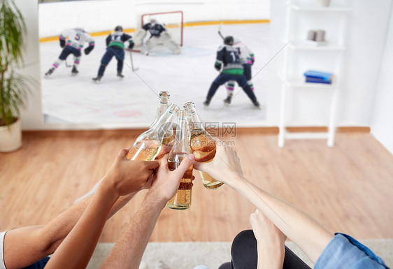 体育娱乐活动人们的快乐的朋友家里的投影仪屏幕上碰碰啤酒瓶看冰球比赛朋友们看冰球喝啤酒图片