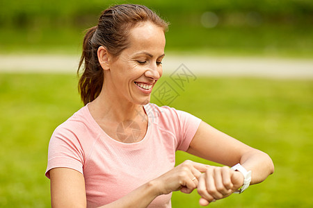 运动技术微笑的女人与智能手表健身跟踪器夏季公园公园里智能手表健身追踪器的女人图片