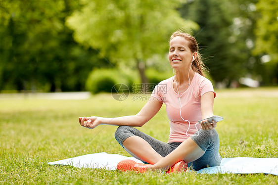 健身,运动技术妇女与智能手机耳机冥想瑜伽垫夏季公园智能手机Hones的女人公园冥想图片