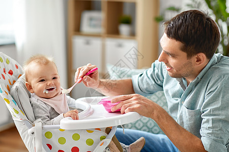 家庭,食物,饮食人的快乐的父亲喂养小婴儿女儿坐高椅子上,用勺子家里父亲家高椅子上喂快乐的婴儿图片