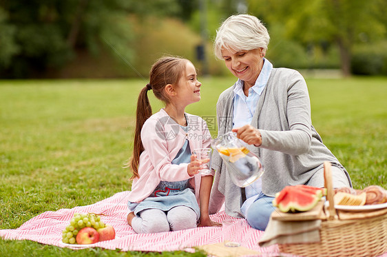 家庭休闲人的快乐的祖母孙女夏季公园野餐喝水果水祖母孙女公园野餐图片