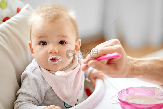 家庭,食物,饮食人的父亲喂养小婴儿坐高椅子上,用勺子家里父亲家里坐高椅子上喂婴儿图片