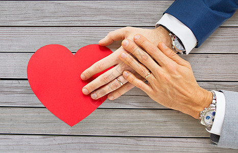 ,同婚姻,情人节爱情亲密的幸福已婚男夫妇的手与红纸心形的桌子上密切的男夫妇的手与红色的心图片
