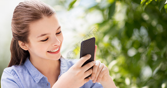 人,技术沟通微笑女孩智能手机上的绿色自然背景快乐的女孩与智能手机自然背景图片
