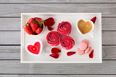 情人节糖果纸杯蛋糕与红色奶油霜,马卡龙,心形咖啡杯,蜡烛草莓白色托盘与玫瑰花瓣灰色木板背景托盘上的款待情人节图片