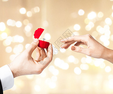 情人节,求婚订婚的男人送钻石戒指小红色礼品盒给女人节日的灯光背景情人节男人给女人钻石戒指图片
