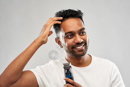修饰人们的微笑的轻印度男子与修剪触摸他的头发灰色的背景微笑的印度男人,修剪者抚摸他的头发图片