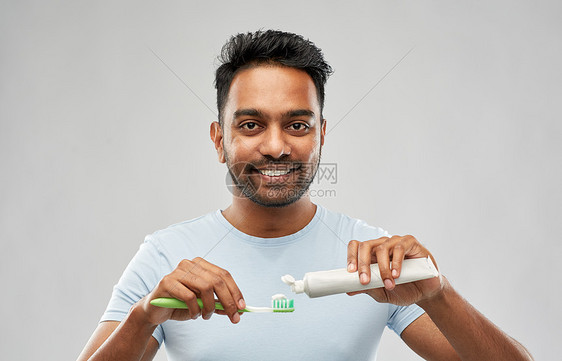 牙齿清洁,牙科护理卫生微笑的轻印度男子牙刷牙膏的灰色背景带牙刷牙膏的印度男人图片