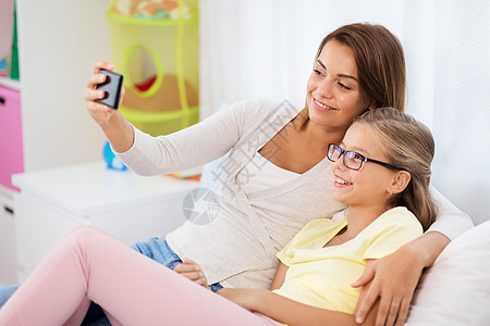 家庭,技术人的快乐的母亲女儿家里用智能手机自拍幸福的家庭家里用智能手机自拍图片