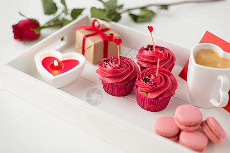 情人节糖果纸杯蛋糕与红色奶油霜心形鸡尾酒棒,马卡龙,蜡烛,咖啡杯礼品盒托盘上情人节的红色糖果图片